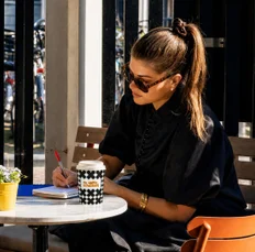 A guest writing at a café table beside a checkerboard cup
