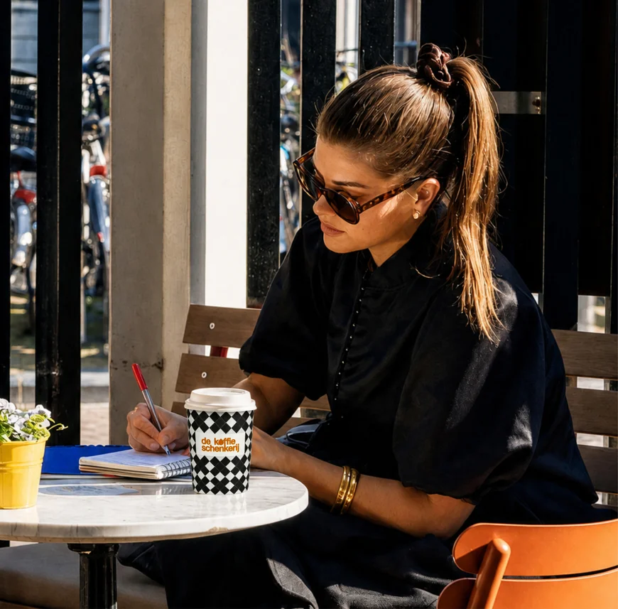 A guest writing at a café table beside a checkerboard cup