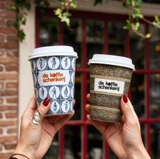 Two cups held up in front of the red-framed shopfront
