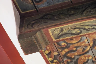 A corner of the painted cornice above the red-panelled wall