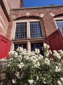 A rebuilt sandstone cross-window today, red shutters open behind flowers