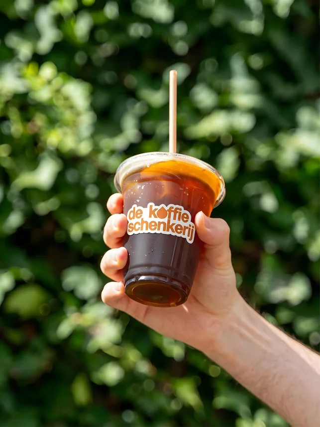 A hand holding an iced coffee against the greenery