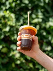 A hand holding an iced coffee against the greenery