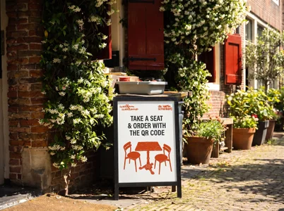 A QR sandwich board in the plant-lined alley beside the Oude Kerk